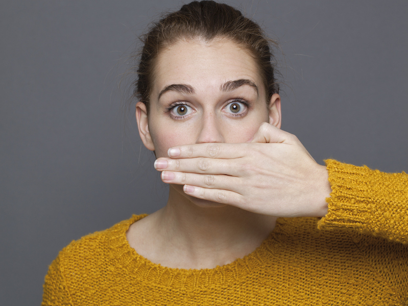 negative feelings concept - portrait of amazed beautiful 20s girl covering her mouth for gag metaphor,studio shot on gray background