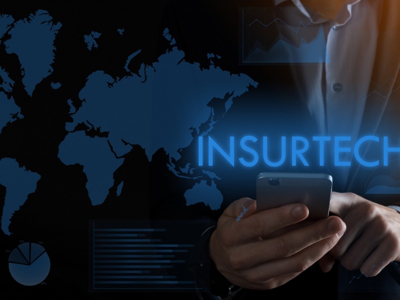 Businessman holding a smartphone with inscription word INSURTECH.