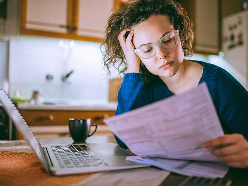 Young brunette curly female reading her bill papers, looking stressed