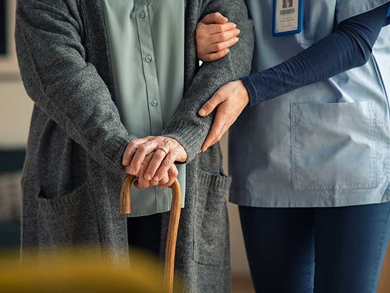 Close up hands of caregiver doctor helping old woman at private clinic. Close up of hands of nurse holding a senior patient with walking stick. Elder woman using walking cane at nursing home with nurse holding hand for support.