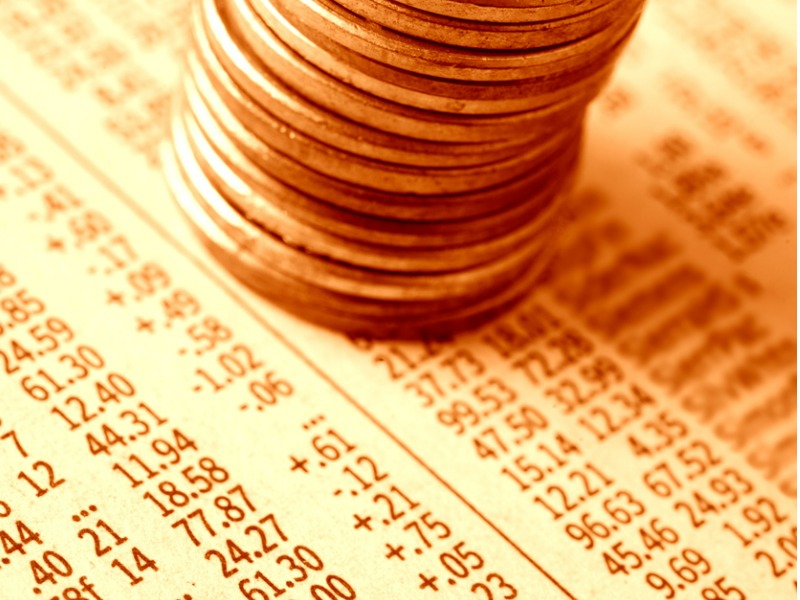 "A stack of pennies on a financial newspaper with stock quotes. Shallow DOF, gold-toned."