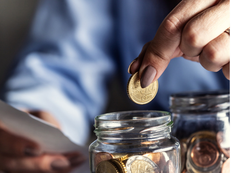 Putting change into a jar of coins by a woman counting bills.
