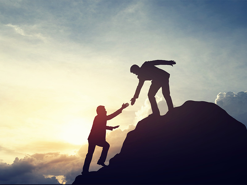 Businessman reaching his hand to help another businessman up a hill.