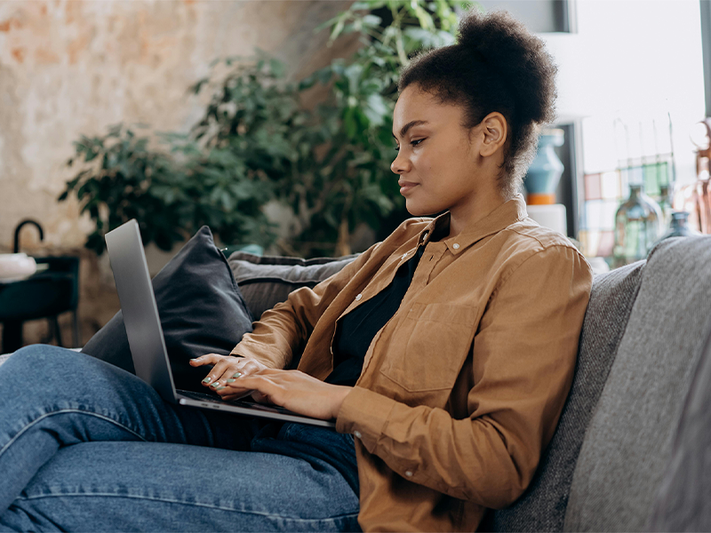 Woman sitting on a couch as she types on her laptop computer