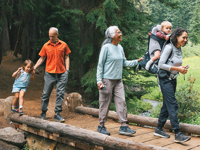 An active and happy multiracial, multigenerational family hike across a small bridge, looking at the beautiful surrounding nature while bonding on a family camping vacation.