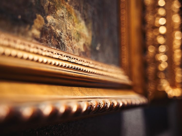 Close-up of an ornate gold picture frame with textured detailing around a painted artwork.