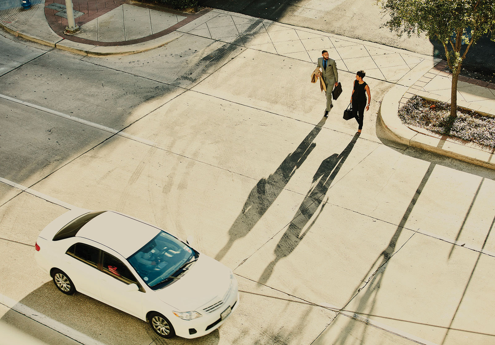 Overhead view of businesswoman and businessman in discussion while walking across city street during early morning commute